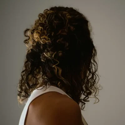 Vrouw met donkerbruin krullend haar en blonde highlights, van achteren gefotografeerd.